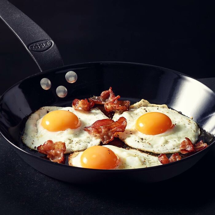 Frying pan with three sunny-side-up eggs and crispy bacon pieces, mouthwatering food photo by Kai Stiepel.