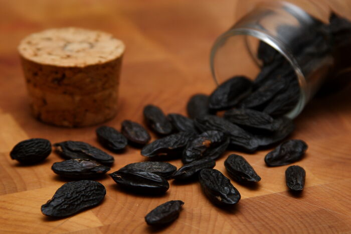 Dried tonka beans spilling from a small glass jar on a wooden surface, an example of foods banned in the USA.
