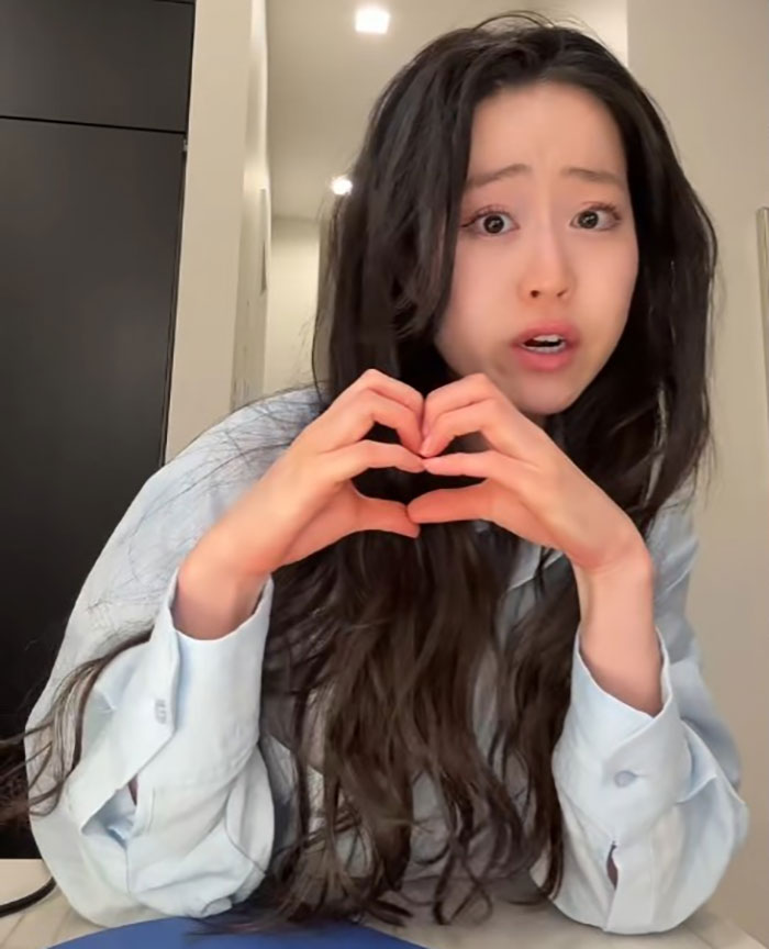 Young woman with long dark hair making a heart shape with her hands, reacting to Diddy's aged look in court. Young woman with long dark hair making a heart shape with her hands, reacting to Diddy's aged look in court.