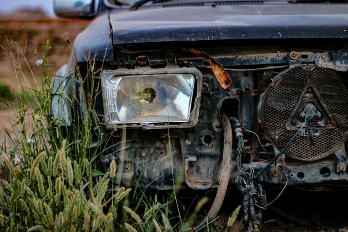 Rusty old car with broken headlight and exposed wiring in tall grass, symbolizing life ruined by one wrong deed.