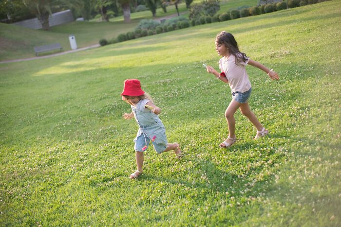 Two young girls running joyfully on a grassy field capturing the essence of baby names that secretly weird them out