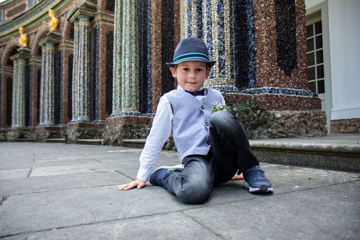 Young boy wearing a hat and vest sitting on pavement by colorful textured columns showcasing acceptable baby names.