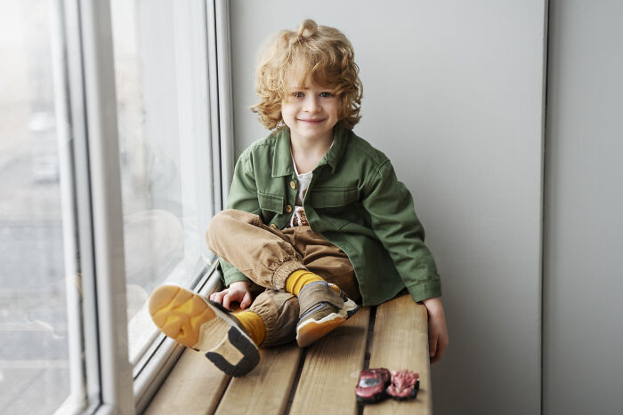 Young child with curly hair sitting by a window, showcasing a relaxed moment related to baby names discussion.
