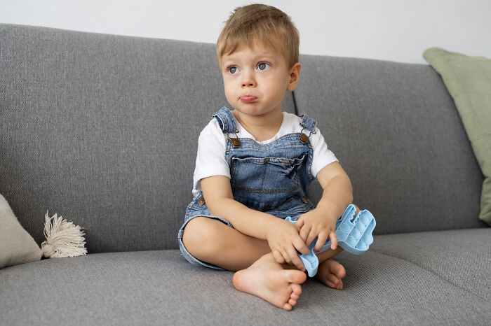 Toddler boy sitting on gray couch holding a blue toy, reflecting on unusual but acceptable baby names.