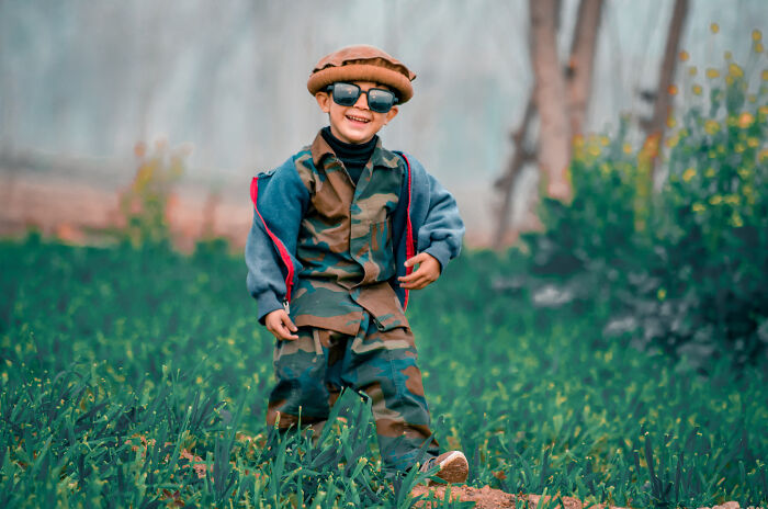 Smiling child wearing camouflage outfit and sunglasses standing outdoors in grass, illustrating unique baby names that weird them out.