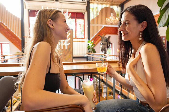Two women smiling and enjoying drinks at a bar during dates that went sour, using the bar’s safe word.