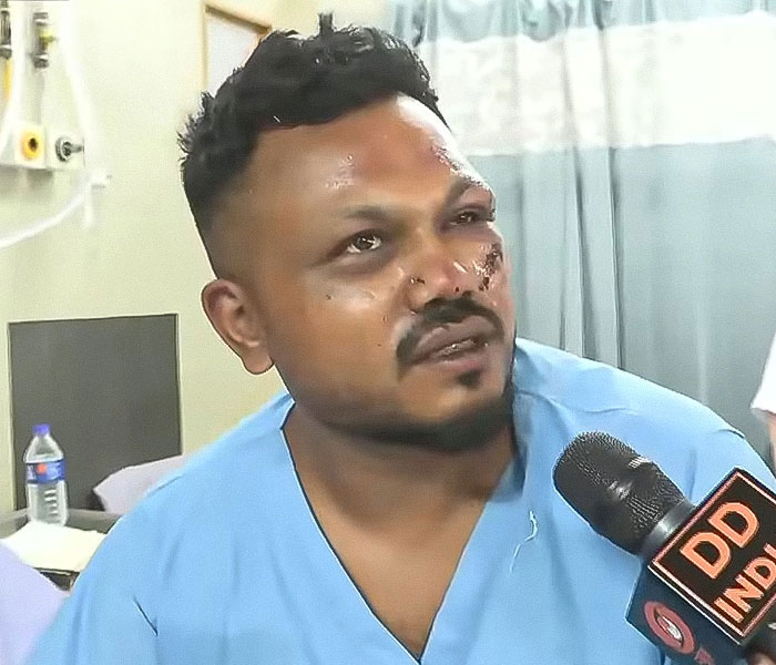 Man with facial injuries wearing hospital gown, speaking to DD India reporter about Air India survivor's guilt.