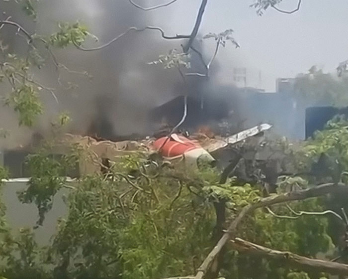 Wreckage of Air India plane crash with smoke rising, surrounded by trees and nearby buildings visible in background. Wreckage of Air India plane crash with smoke rising, surrounded by trees and nearby buildings visible in background.