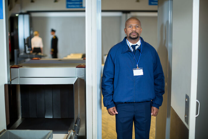 TSA agent standing by security checkpoint to help travelers avoid being held up in security line before boarding. TSA agent standing by security checkpoint to help travelers avoid being held up in security line before boarding.