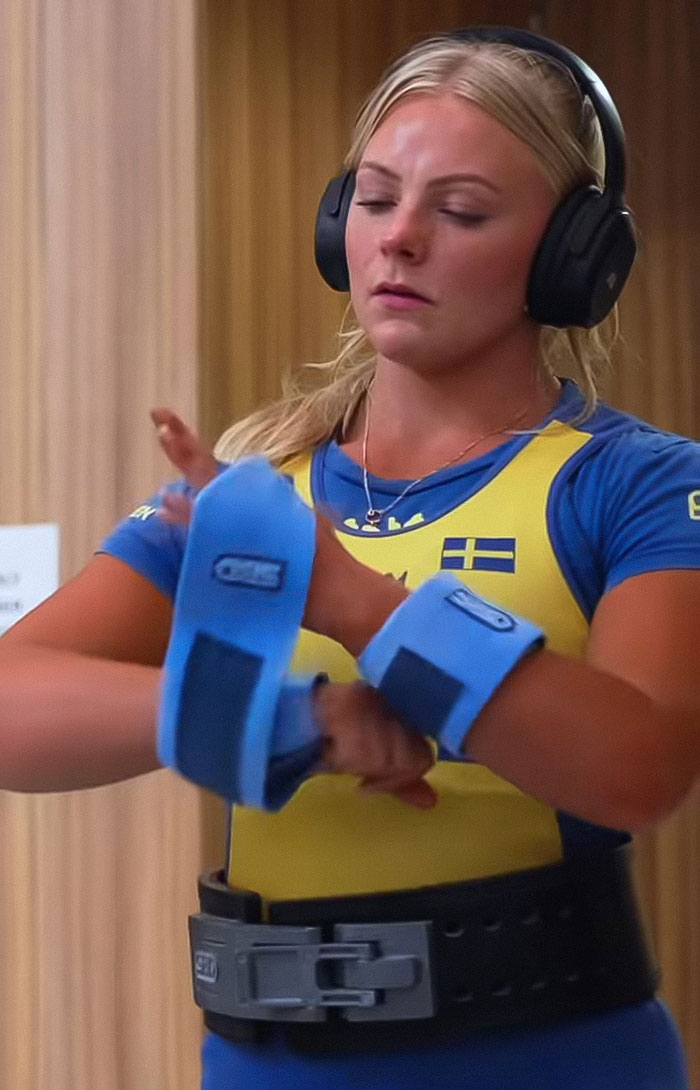 Female powerlifter wearing wrist wraps and headphones, preparing mentally before a competition performance. Female powerlifter wearing wrist wraps and headphones, preparing mentally before a competition performance.