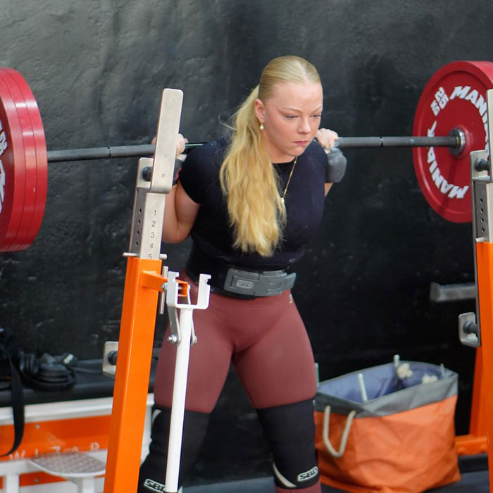 Woman powerlifting in competition, preparing to lift a heavy barbell on her shoulders during the event. Woman powerlifting in competition, preparing to lift a heavy barbell on her shoulders during the event.