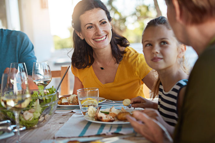Woman in yellow top smiling at family dinner while discussing solo traveler expected to stop drinking alcohol. Woman in yellow top smiling at family dinner while discussing solo traveler expected to stop drinking alcohol.