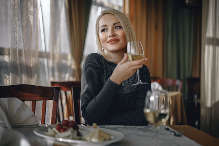 Solo female traveler enjoying a glass of white wine at a restaurant, highlighting women drinking while traveling. Solo female traveler enjoying a glass of white wine at a restaurant, highlighting women drinking while traveling.