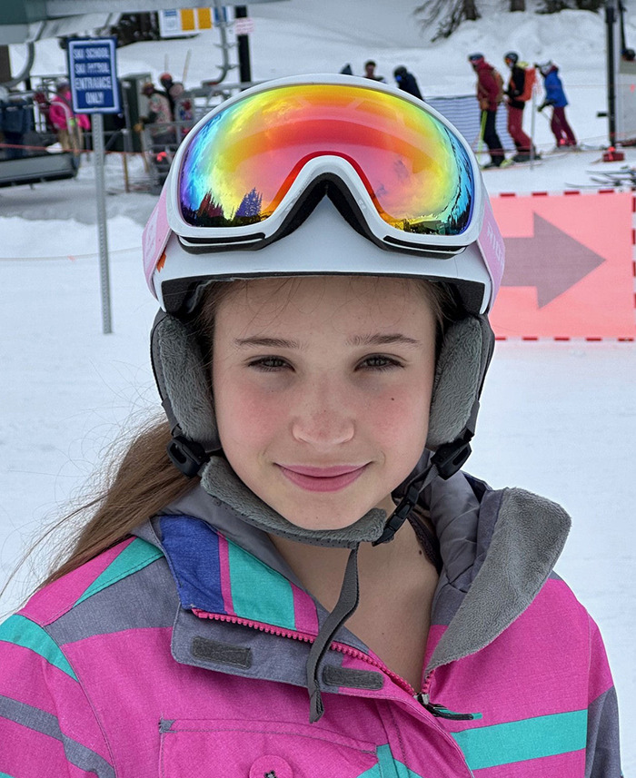 Teen girl smiling in ski gear with helmet and reflective goggles during a snowy day at a ski resort. Teen girl smiling in ski gear with helmet and reflective goggles during a snowy day at a ski resort.