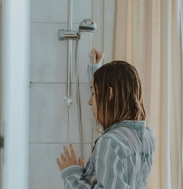 Woman in striped shirt standing under running shower, showing cold shower as a memory reminder gesture. Woman in striped shirt standing under running shower, showing cold shower as a memory reminder gesture.
