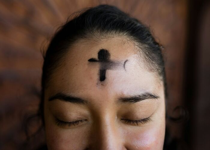 Close-up of a person with eyes closed and a smudged ash cross on forehead symbolizing one wrong deed consequences.