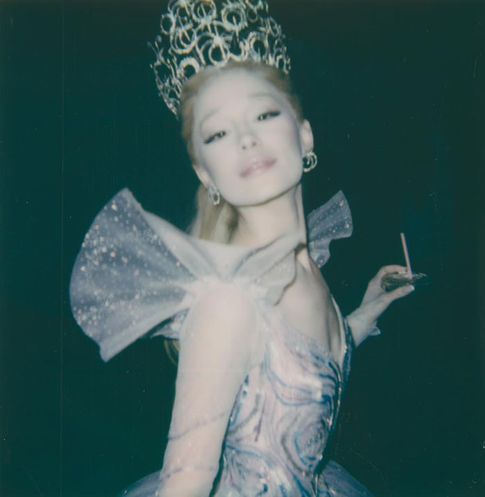 Ariana Grande wearing a sparkling costume with an ornate headpiece in a dark setting, highlighting her entirely visible ribcage look. Ariana Grande wearing a sparkling costume with an ornate headpiece in a dark setting, highlighting her entirely visible ribcage look.