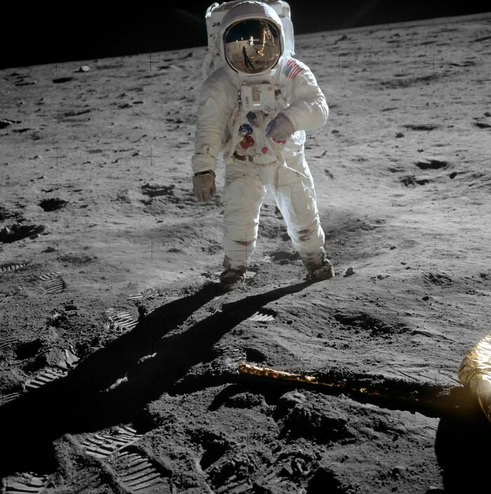 Apollo mission astronaut standing on the moon surface with footprints and lunar equipment casting long shadows.
