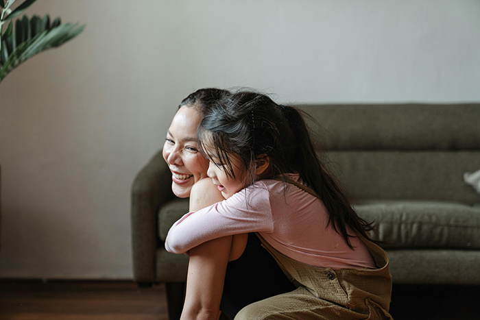 Young mom smiling and hugging her child in a living room, illustrating family dynamics and legacy challenges.