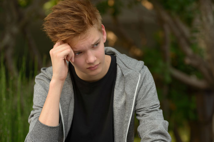 Teen boy looking worried outdoors, reflecting concerns about babysitting autistic stepbrother and refusing related classes. Teen boy looking worried outdoors, reflecting concerns about babysitting autistic stepbrother and refusing related classes.