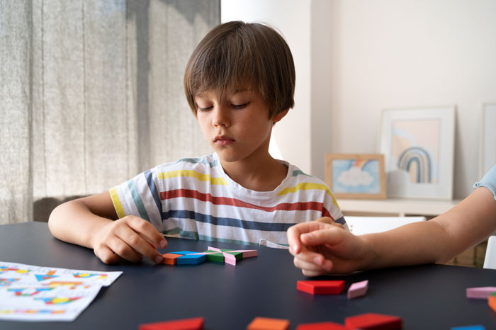 Teen boy working with colorful puzzle pieces, highlighting challenges of babysitting autistic stepbro in home setting.