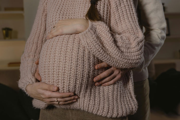 Pregnant woman wearing pink sweater with hands on belly, illustrating MIL convinced baby gender was manipulated conflict. Pregnant woman wearing pink sweater with hands on belly, illustrating MIL convinced baby gender was manipulated conflict.