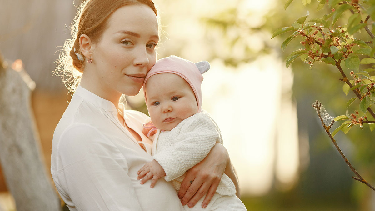 Young mother holding baby outdoors at sunset, reflecting tension around MIL convinced pregnant DIL manipulated babyu2019s gender.