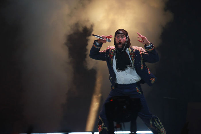 Bad Bunny performing on stage with microphone, showcasing energy and style related to net worth and WWE events.