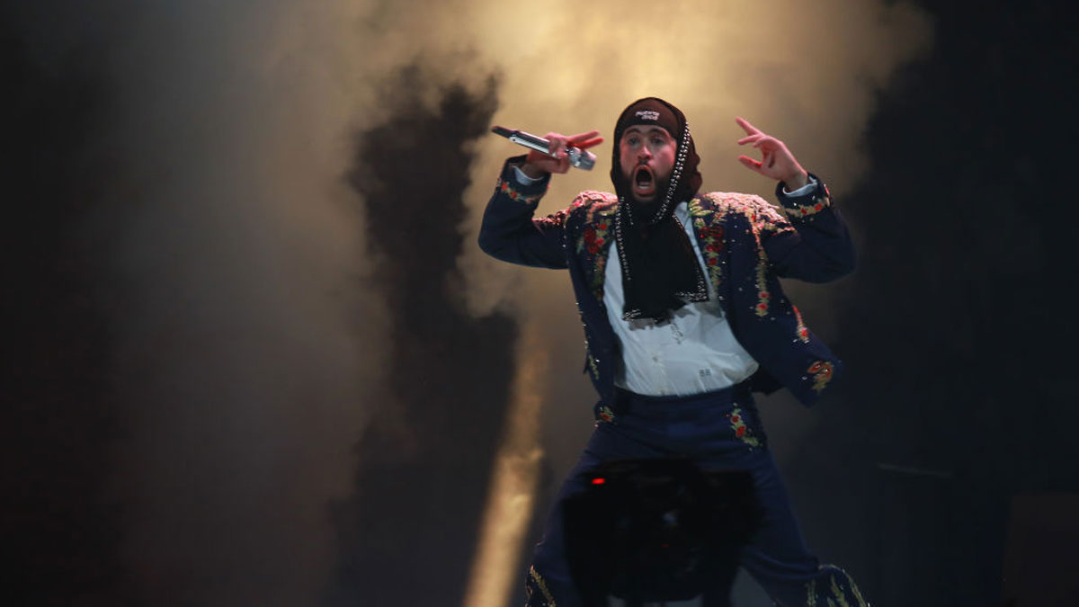 Bad Bunny performing on stage with energetic gestures and smoke effects highlighting his net worth and career.