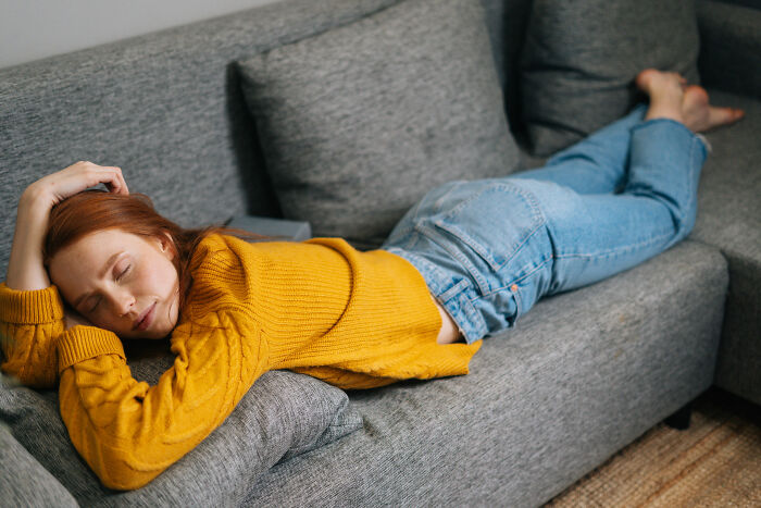 Young woman lying on gray couch with eyes closed, reflecting on bad things people face in life and struggles.