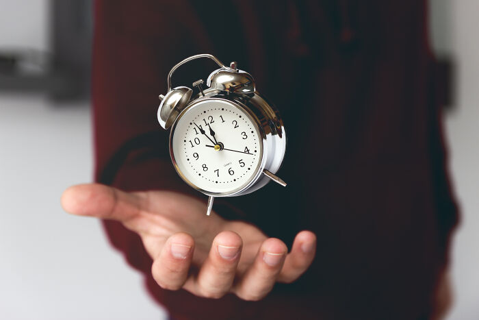 Hand holding a small silver alarm clock, symbolizing bad things people experience in life and limited time.