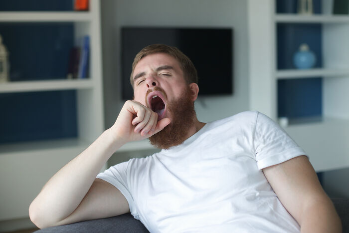 A tired man yawning on a couch indoors, illustrating bad things people face in life and daily struggles.