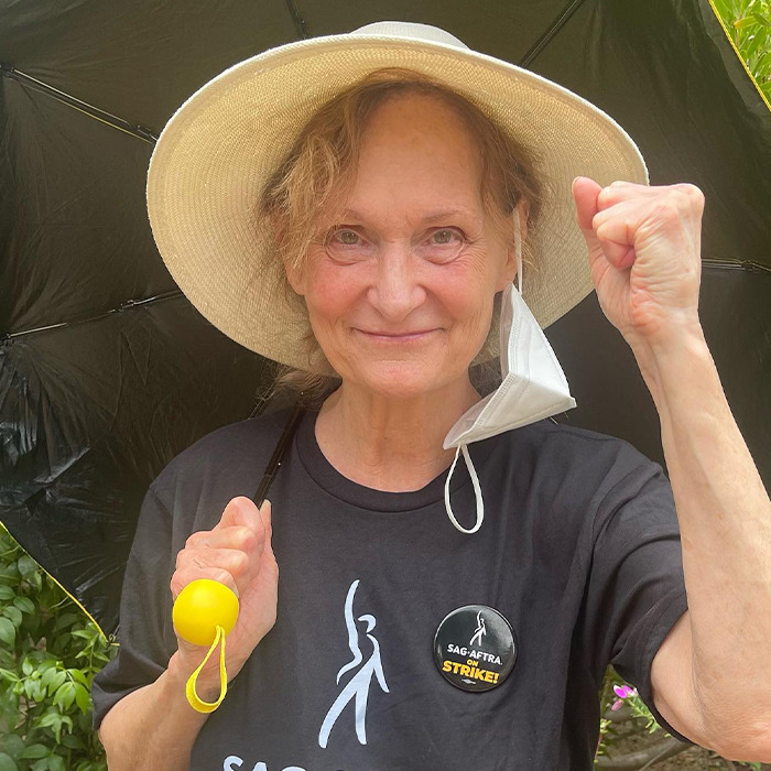 Beloved ’90s star and Rain Man co-star wearing a hat and a strike button, raising fist outdoors. Beloved ’90s star and Rain Man co-star wearing a hat and a strike button, raising fist outdoors.