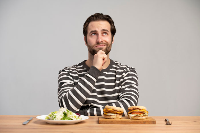 Man in a striped shirt deciding between best processed foods and a healthy salad for weight loss at a wooden table Man in a striped shirt deciding between best processed foods and a healthy salad for weight loss at a wooden table