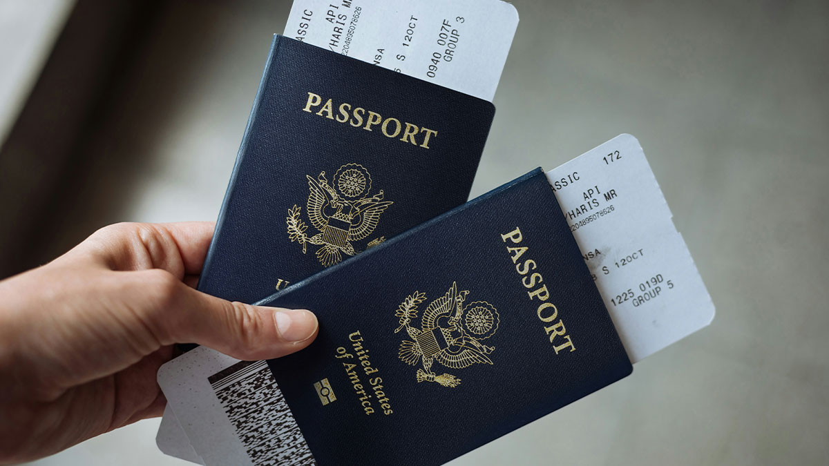 Hand holding two US passports with plane tickets, representing the best time to buy plane tickets for cheapest airfare.