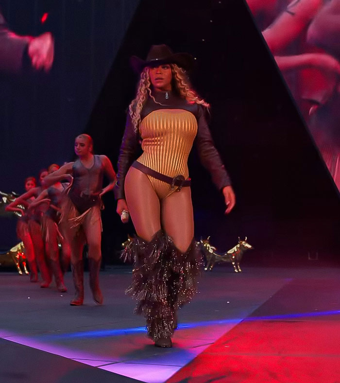 Beyoncé performing on stage wearing a cowboy hat and fringed boots during a show with dance backup.