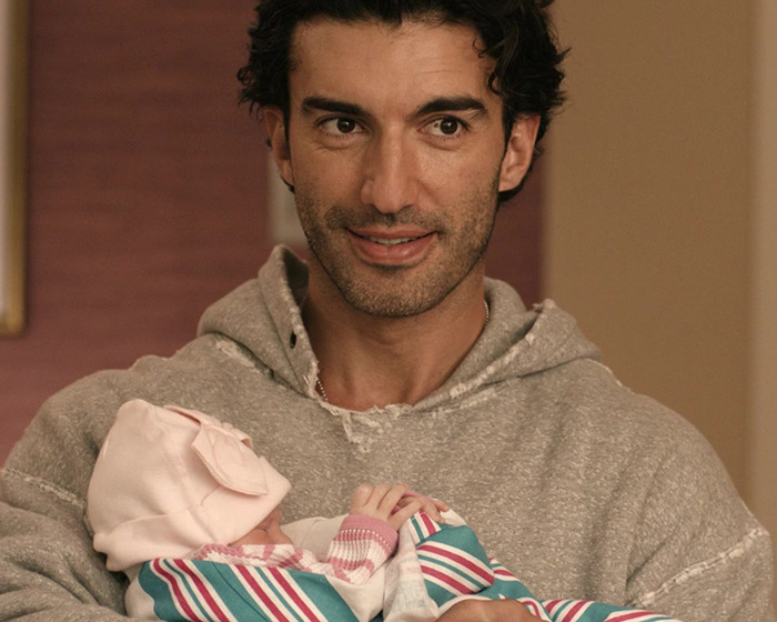 Man in gray hoodie smiling while holding newborn baby wrapped in a striped blanket indoors. Man in gray hoodie smiling while holding newborn baby wrapped in a striped blanket indoors.