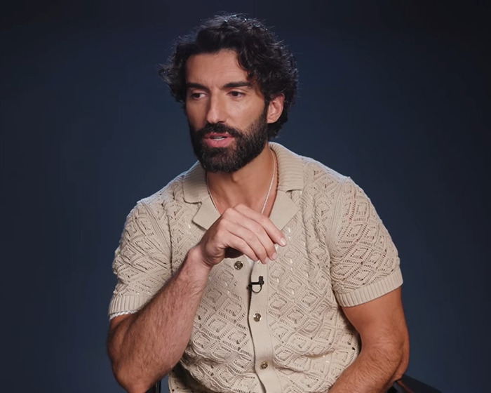 Man with dark curly hair and beard wearing beige patterned short sleeve shirt speaking in a studio setting involving Blake Lively lawsuit Man with dark curly hair and beard wearing beige patterned short sleeve shirt speaking in a studio setting involving Blake Lively lawsuit