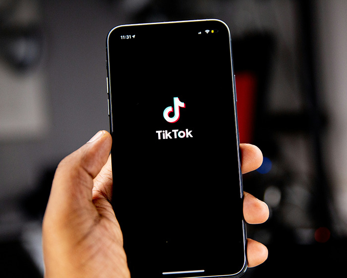 Hand holding smartphone displaying TikTok app, related to viral scarf challenge involving boy aged 12 safety concerns. Hand holding smartphone displaying TikTok app, related to viral scarf challenge involving boy aged 12 safety concerns.