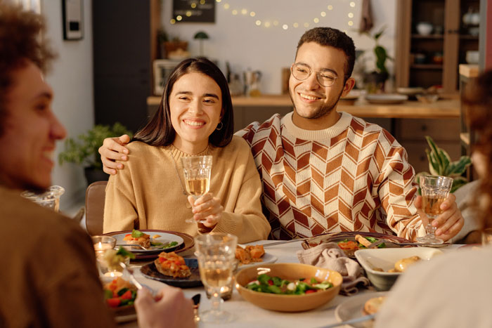 Young woman with boyfriend at dinner, smiling nervously while meeting boyfriend’s mom and facing subtle comparisons.