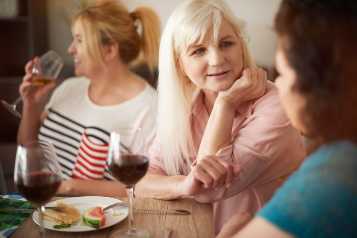 Middle-aged woman listening intently while another woman drinks wine, highlighting conflict with boyfriend’s mom and comparisons.