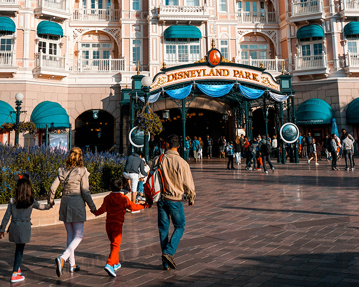 Family walking towards entrance of Disneyland Park on a sunny day with crowds gathered at the entrance. Family walking towards entrance of Disneyland Park on a sunny day with crowds gathered at the entrance.