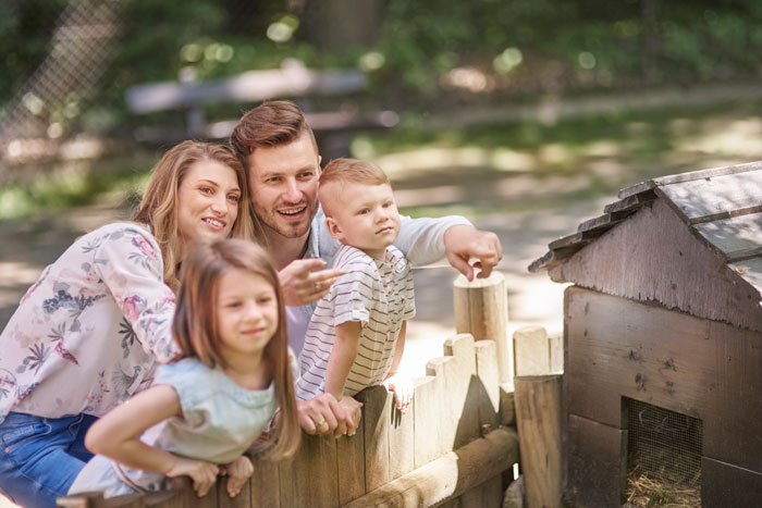 Family gathering outside near a wooden fence with a man, woman, and two children enjoying time together. Family gathering outside near a wooden fence with a man, woman, and two children enjoying time together.
