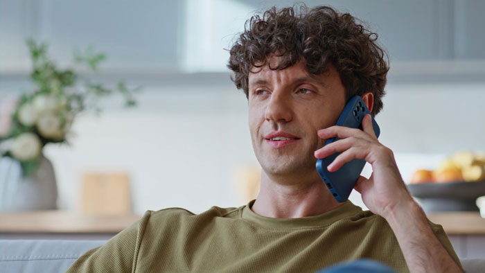 Man with curly hair reclining on couch, talking on phone, reflecting tension in family after brother’s lie to CPS incident. Man with curly hair reclining on couch, talking on phone, reflecting tension in family after brother’s lie to CPS incident.