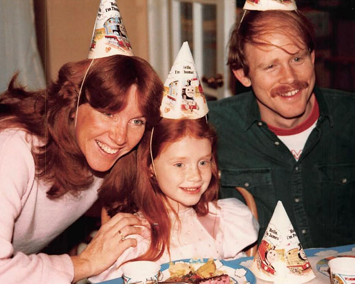 Family celebrating a birthday with Bryce Dallas Howard as a child wearing party hats in a vintage photo capturing her childhood memory. Family celebrating a birthday with Bryce Dallas Howard as a child wearing party hats in a vintage photo capturing her childhood memory.
