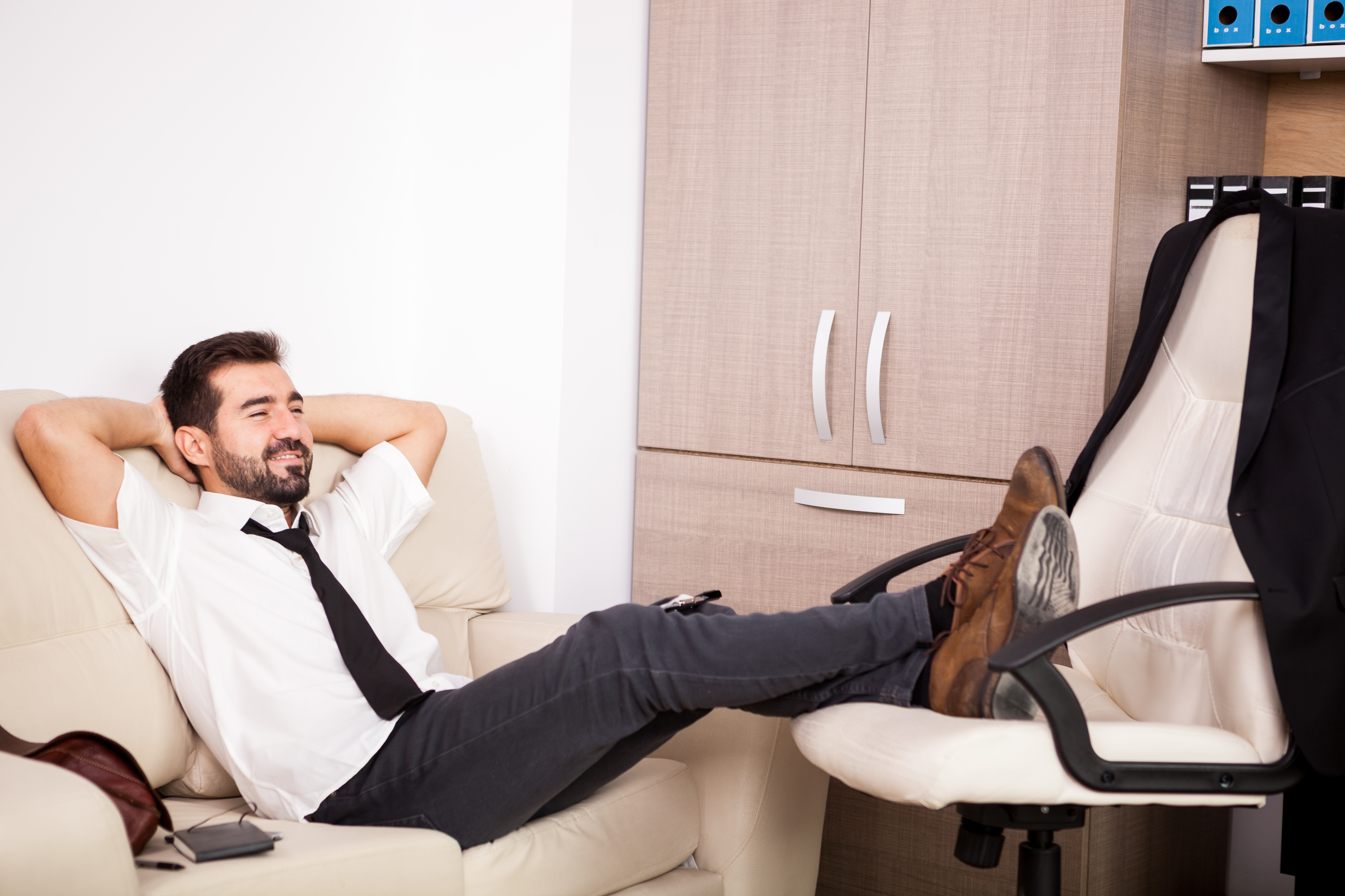 Man in casual outfit reclining on a couch with feet on chair, highlighting stereotypical American style conflict in photos. Man in casual outfit reclining on a couch with feet on chair, highlighting stereotypical American style conflict in photos.