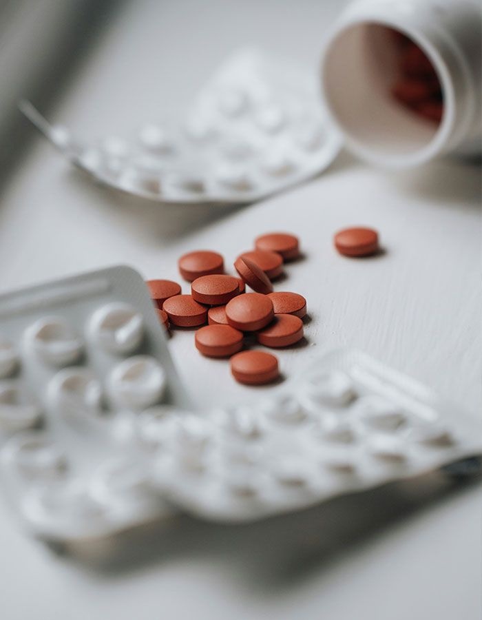 Red caffeine tablets spilled on white surface with blurred white pill blister packs and bottle in background. Red caffeine tablets spilled on white surface with blurred white pill blister packs and bottle in background.
