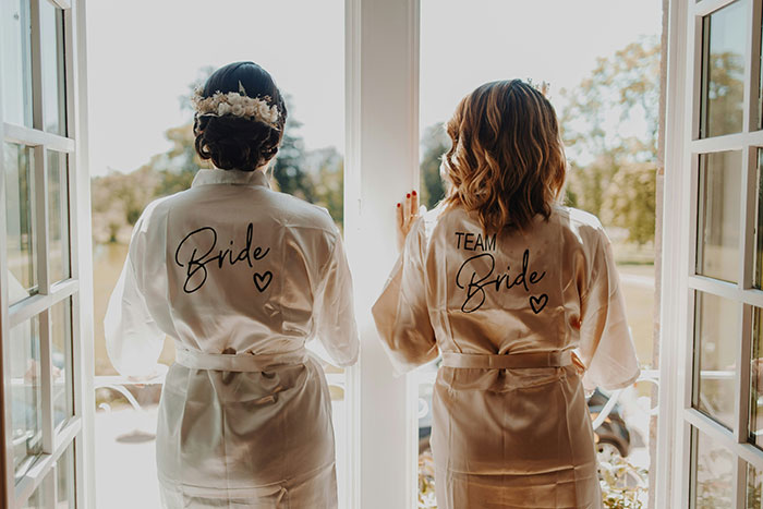 Bride and maid of honor standing by open doors, wearing robes, highlighting psoriasis and wedding body makeup conflict. Bride and maid of honor standing by open doors, wearing robes, highlighting psoriasis and wedding body makeup conflict.
