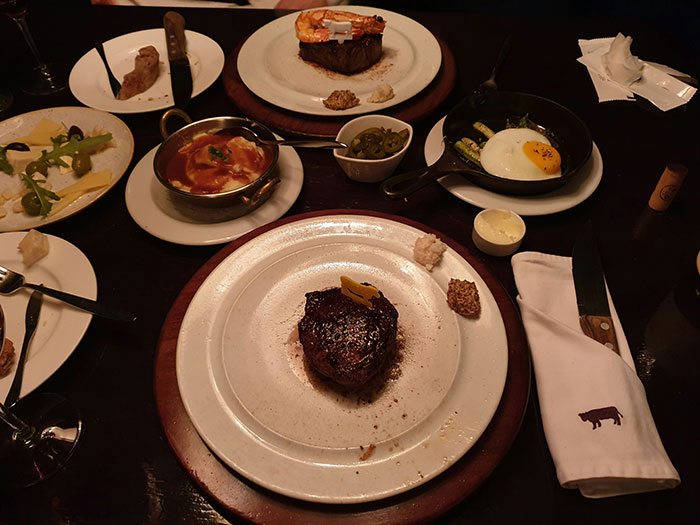 Steak dinner with shrimp, fried egg, and side dishes on a dark table, illustrating a Vegas night food experience. Steak dinner with shrimp, fried egg, and side dishes on a dark table, illustrating a Vegas night food experience.