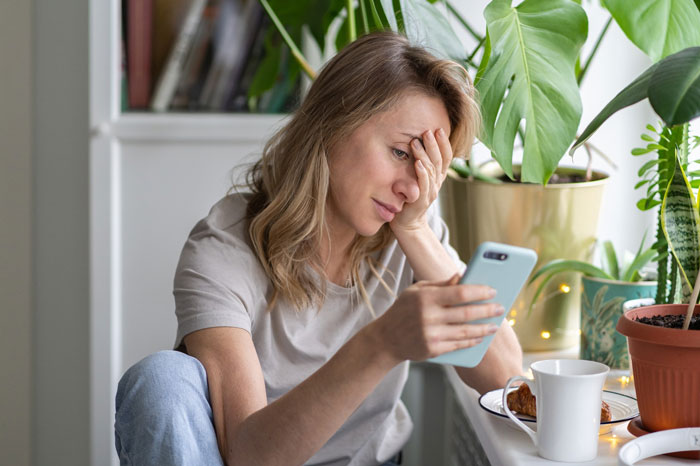 Woman stressed while reading phone, reflecting on venue host sending $1200 cleaning bill after event. Woman stressed while reading phone, reflecting on venue host sending $1200 cleaning bill after event.